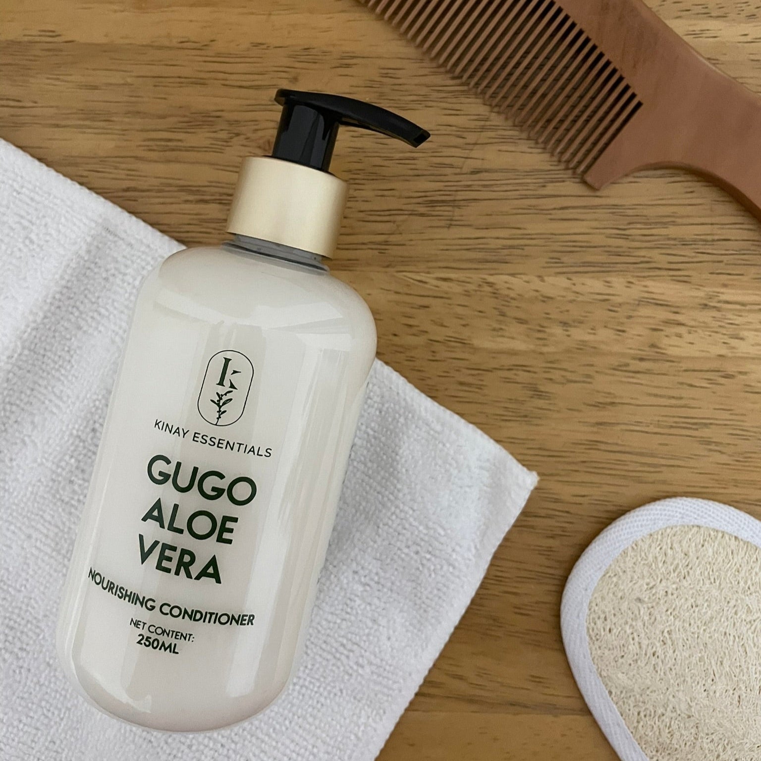 Gugo Aloe Vera conditioner bottle with a wooden comb and a small loofah on a wooden surface.