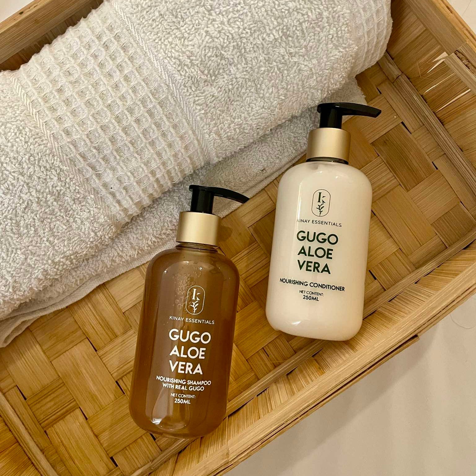 Two bottles of Gugo Aloe Vera products on a woven tray with a towel.