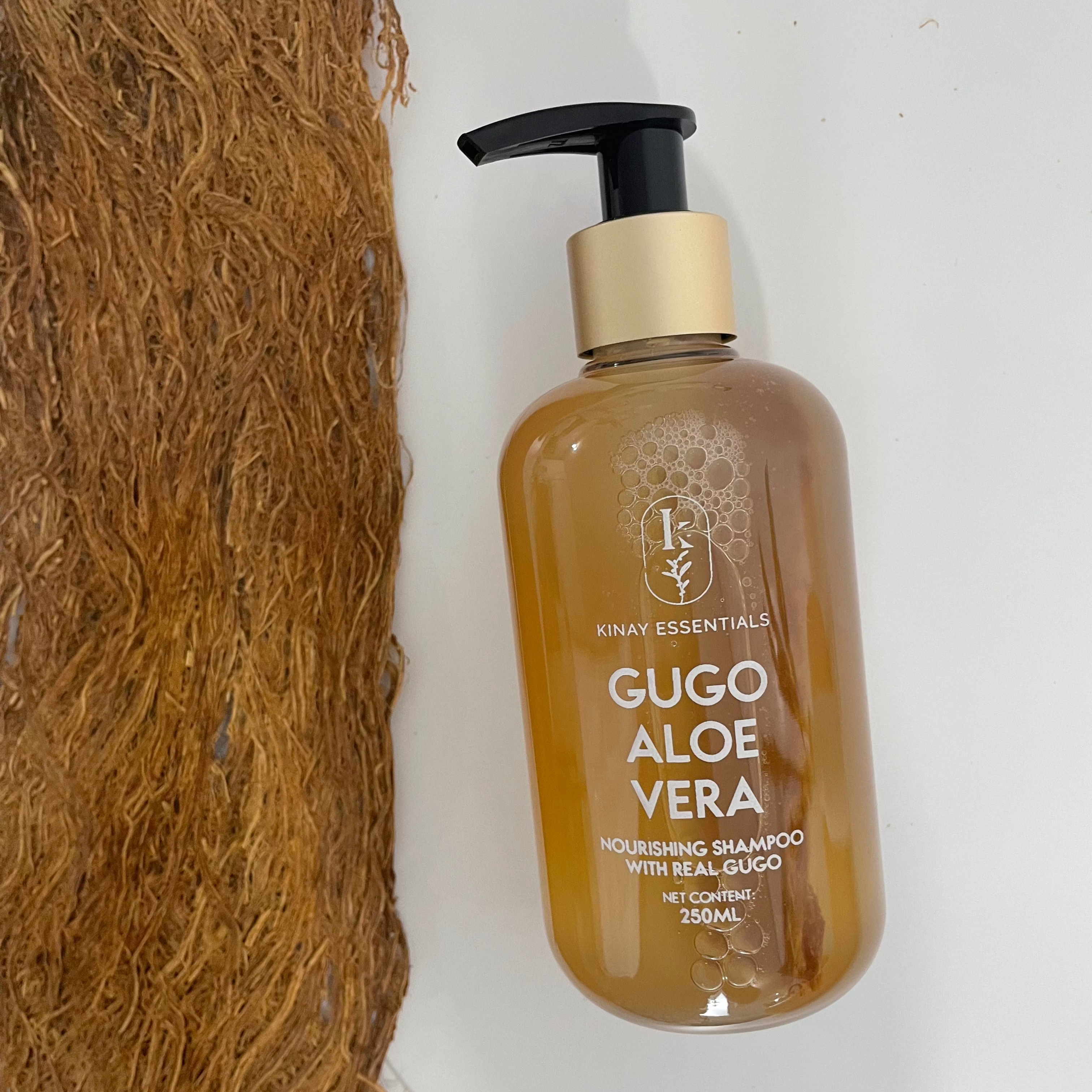 Bottle of Gugo Aloe Vera shampoo next to a piece of gugo bark on a white background