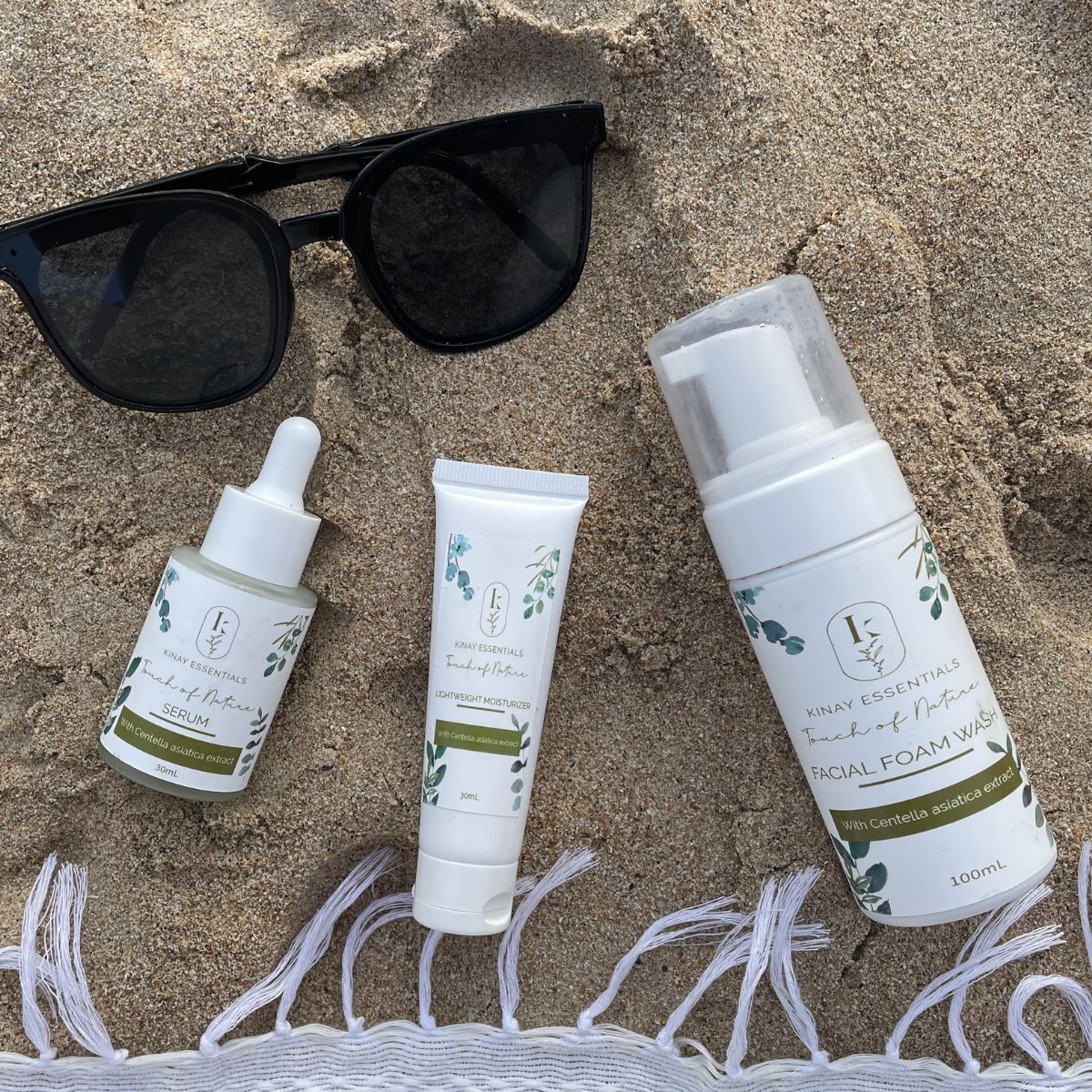Skincare products and sunglasses on sand with a towel