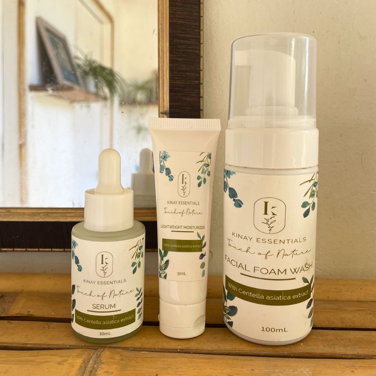 Three skincare products from Kinay Essentials on a wooden surface with a mirror in the background.